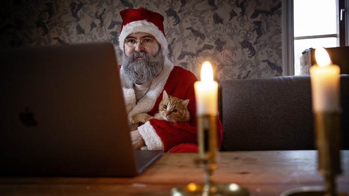 Tomten Tobias Guldstrand har sprayat skägget vitt och sitter redo vid datorn tillsammans med katten Findus.
