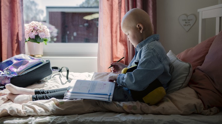 Alice sitter i sin s&auml;ng med en skolbok och penna i kn&auml;t