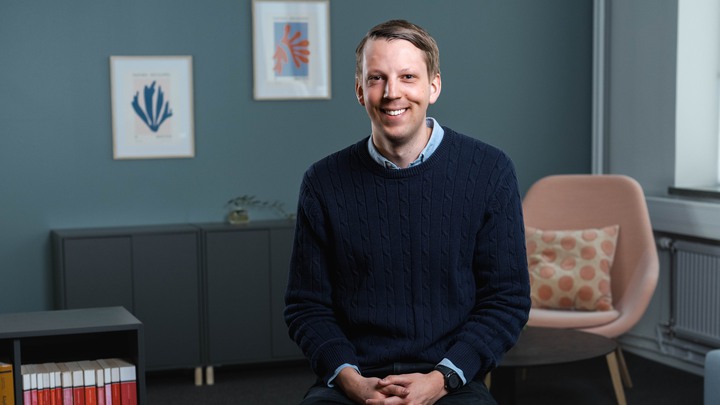 Ung man i kontorsmilj&ouml; som ler mot kameran