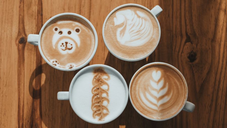 Fyra kaffekoppar med olika motiv i skummad mjölk, bland annat ett lejon samt olika växtmotiv.
