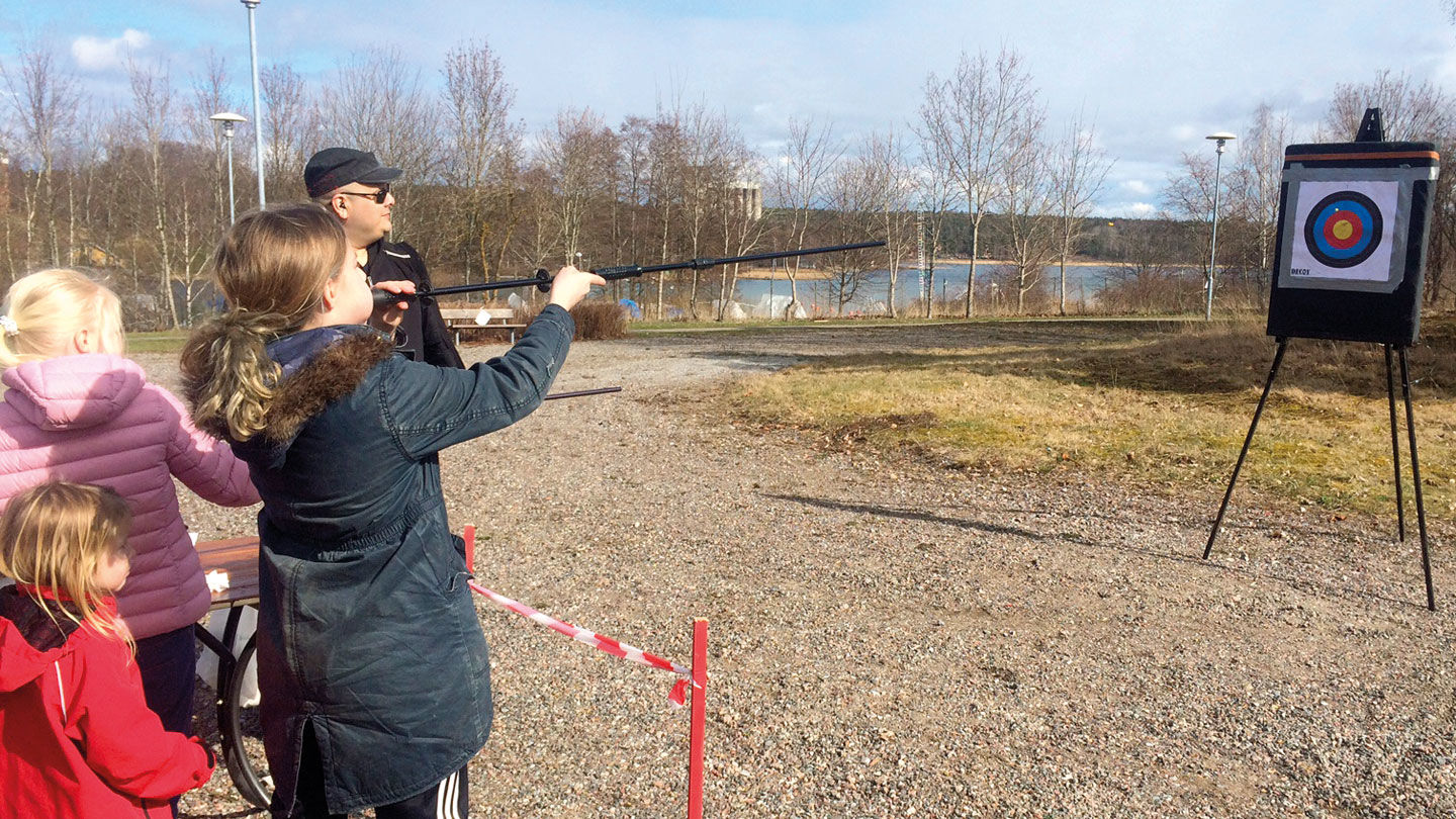 Ett barn skjuter prick med blåsrör utomhus.