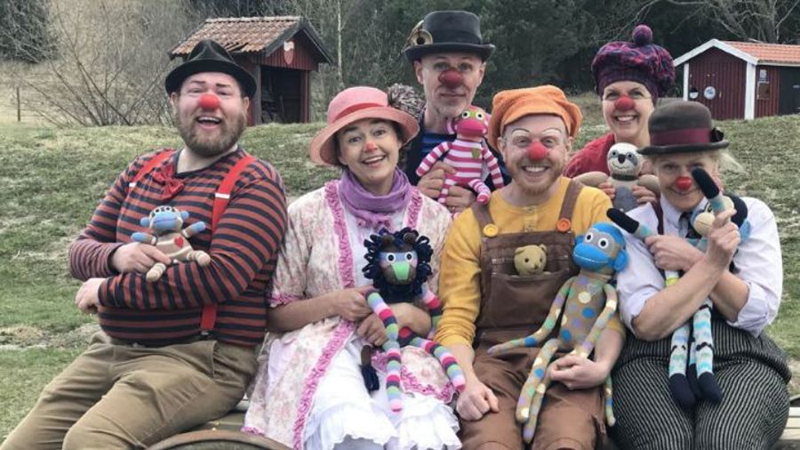 Sex glada clowner sittande med gosedjur i famnen på bänk utomhus