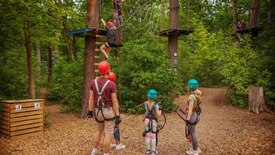 En vuxen och två barn tittar på en som klättrar i start på höghöjdsbana.